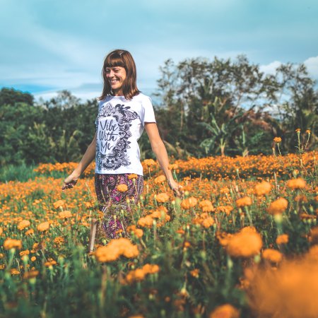 Vrouw in een bloemenveld in de natuur met 'Vibe with me' op haar T-shirt (Foto: Artem Bali / Unsplash)
